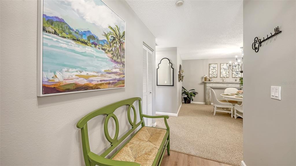 A hallway with a green bench and wall art leads to a dining room area — 3500 EL CONQUISTADOR PARKWAY UNIT 148, BRADENTON, FL