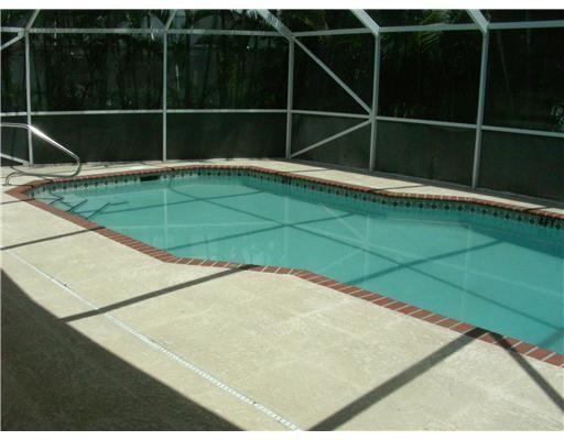 A rectangular swimming pool with a brick border is enclosed by a white screen cage — 19600 Sea Pines Way, Boca Raton FL 33498, BOCA RATON, FL