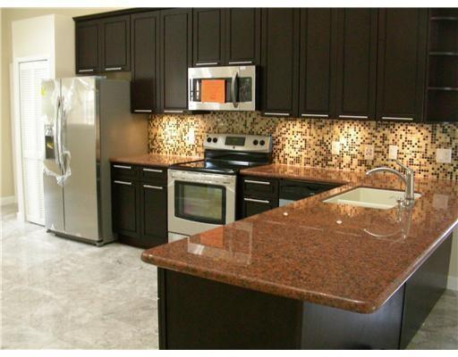 A kitchen with dark wood cabinets, stainless steel appliances, and red granite countertops — 19600 Sea Pines Way, Boca Raton FL 33498, BOCA RATON, FL