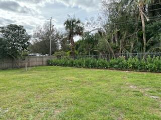 A grassy backyard features a wooden fence, a row of hedges, and mature trees — 4404 SE Mulford Lane, Stuart FL 34997, STUART, FL