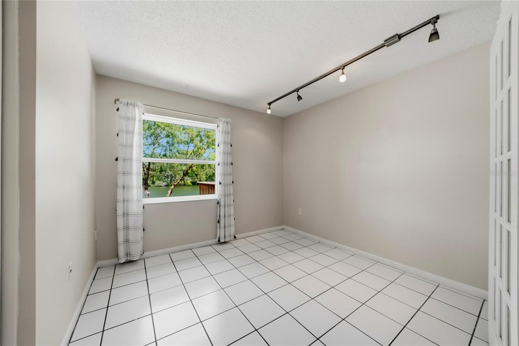 An empty room with white tiled floors, track lighting, and a window overlooking a lake — 906 CARLTON ROAD, TARPON SPRINGS, FL