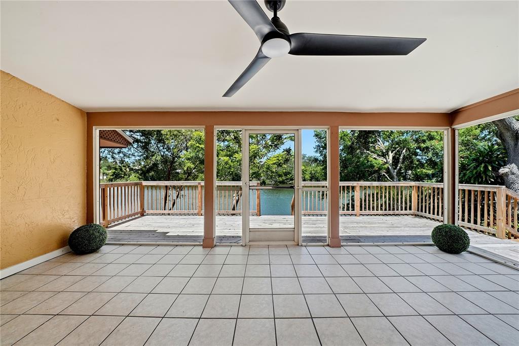 A tiled screened-in porch features a ceiling fan and a wooden deck overlooking a lake — 906 CARLTON ROAD, TARPON SPRINGS, FL