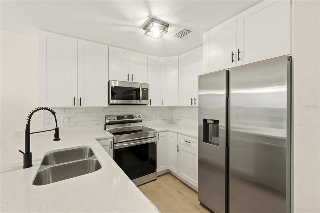 A modern kitchen features white cabinets, stainless steel appliances, and white countertops — 205 SOMERSET LANE, PALM HARBOR, FL