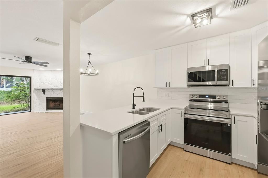 A modern kitchen with white cabinets, stainless steel appliances, and a peninsula sink — 205 SOMERSET LANE, PALM HARBOR, FL
