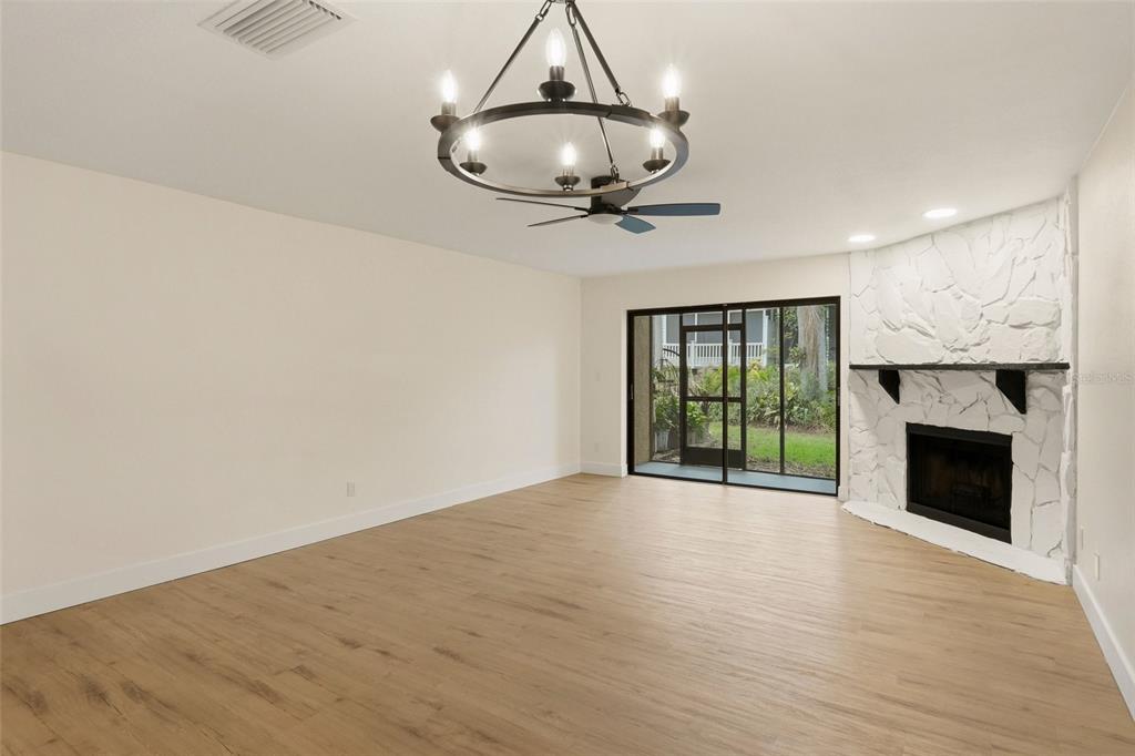 A living room with light wood flooring, a chandelier, and a white stone corner fireplace — 205 SOMERSET LANE, PALM HARBOR, FL