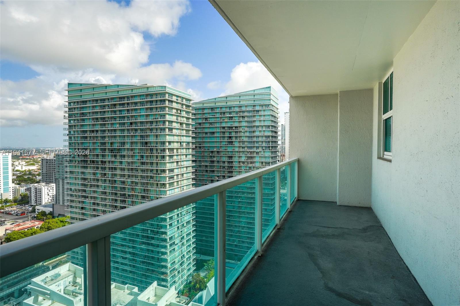 A balcony with a glass railing overlooks two large, modern glass skyscrapers under a blue sky — 1250 S Miami Ave # 3003, Miami FL 33130, MIAMI, FL