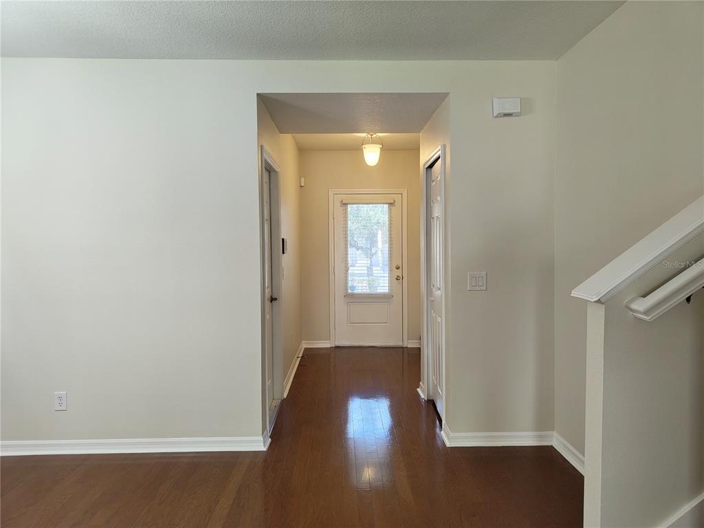 A foyer with hardwood floors leads to a white front door under a pendant light — 2023 LACIE JO LANE, KISSIMMEE, FL