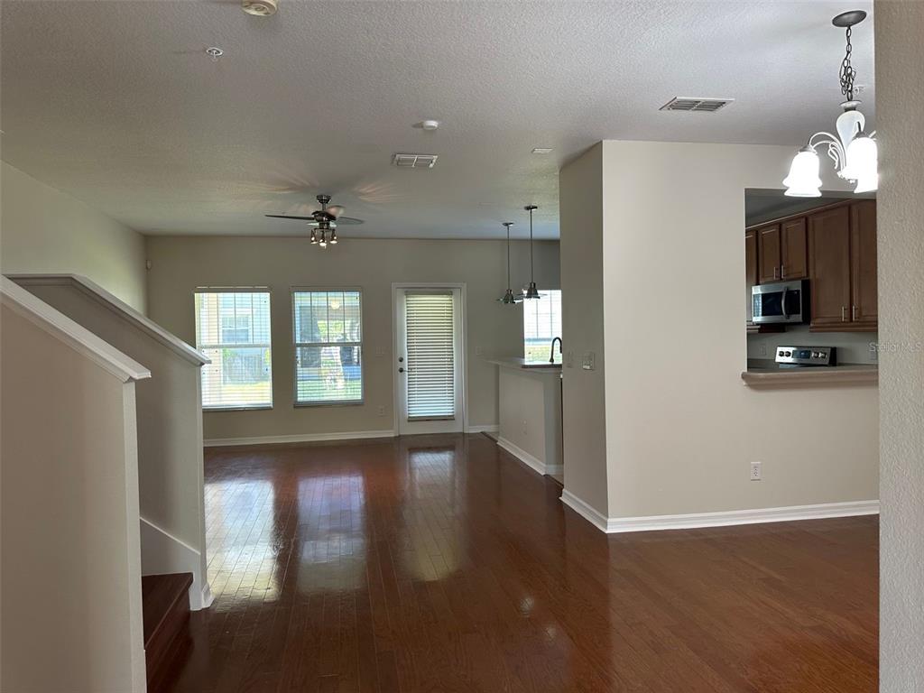 A living area with hardwood floors, a staircase, and an open kitchen with dark cabinets — 2023 LACIE JO LANE, KISSIMMEE, FL