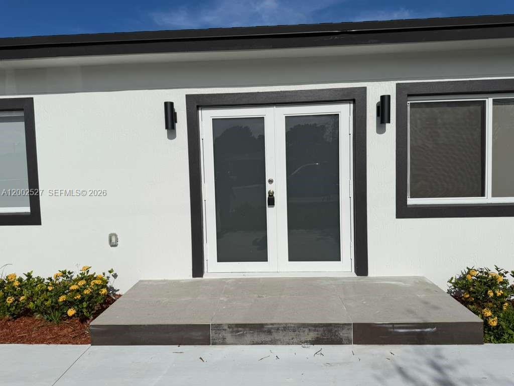 A white exterior wall features a double glass door entry and a tiled porch — 831 SE 9th Ave, Hialeah FL 33010, HIALEAH, FL