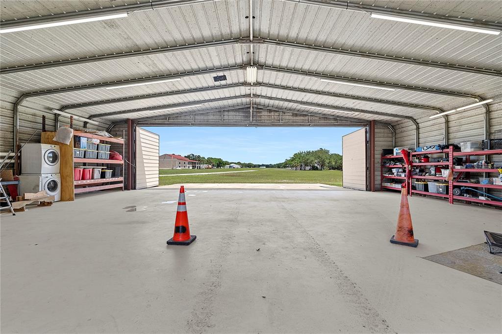 A large, open-air metal hangar features concrete floors, storage shelving, and a view of a field — 1851 MAYTOWN ROAD, OAK HILL, FL
