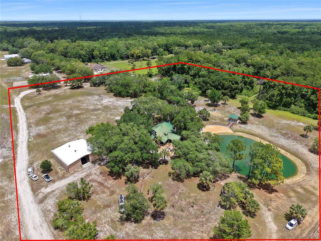 An aerial view shows a house, a large metal barn, and a pond on property — 1851 MAYTOWN ROAD, OAK HILL, FL