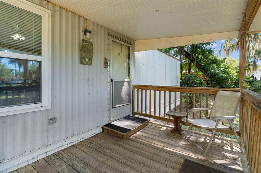 A wooden porch with a railing, a chair, and a small table outside a home — 5891 SE 145TH STREET, SUMMERFIELD, FL