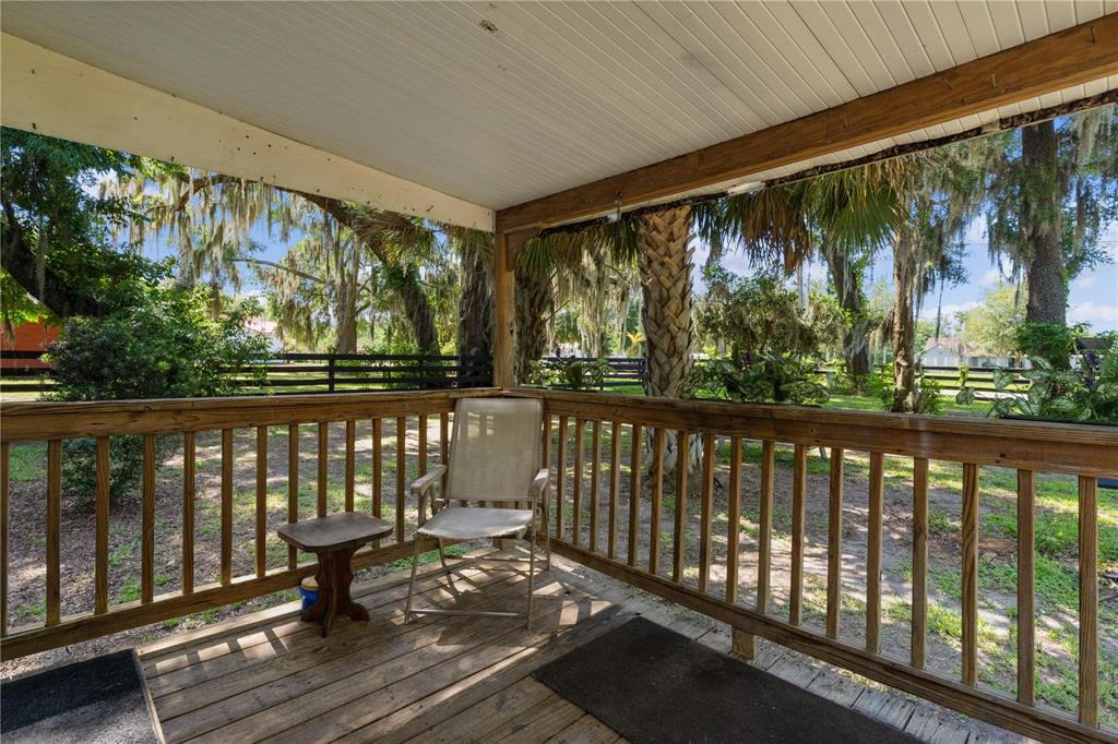 A covered wooden porch features a railing, a single chair, and a small side table — 5891 SE 145TH STREET, SUMMERFIELD, FL