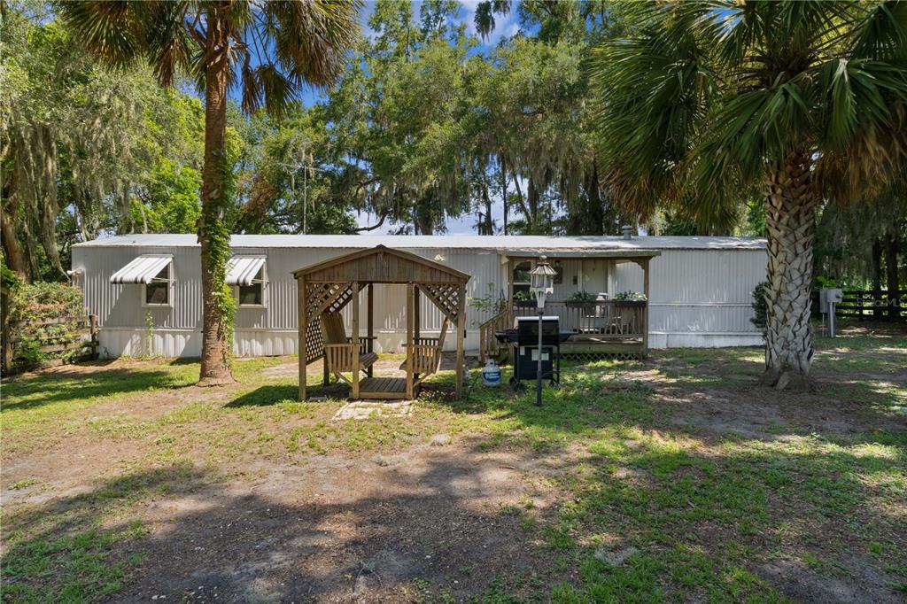 A single-wide mobile home with a wooden gazebo and a small porch in a yard — 5891 SE 145TH STREET, SUMMERFIELD, FL