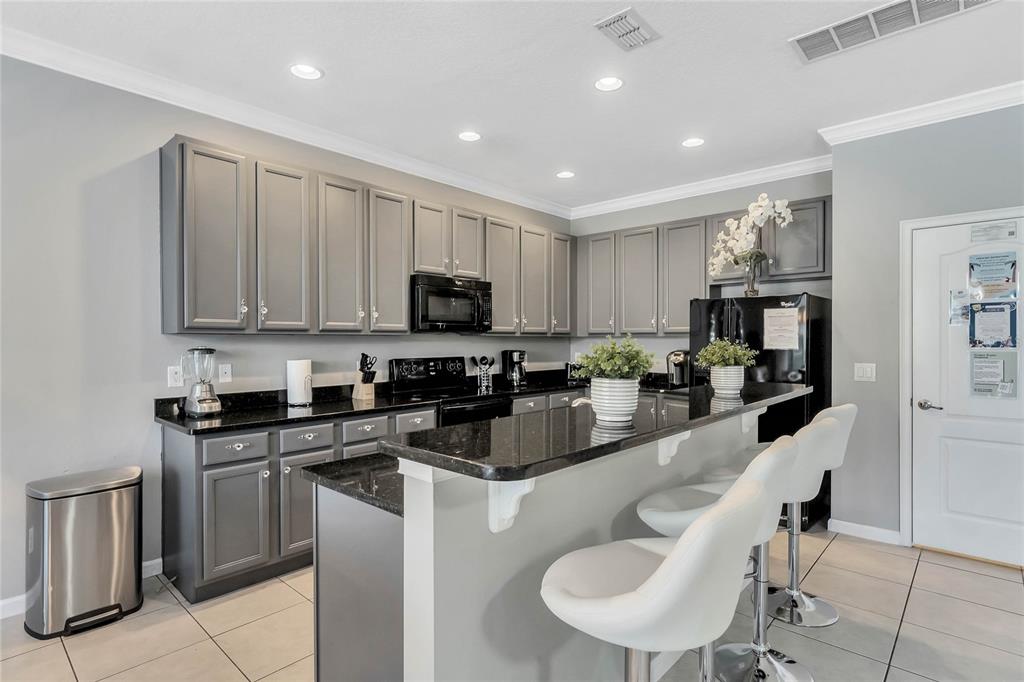 A kitchen features gray cabinets, black granite countertops, a breakfast bar, and white bar stools — 4348 ACORN COURT, DAVENPORT, FL