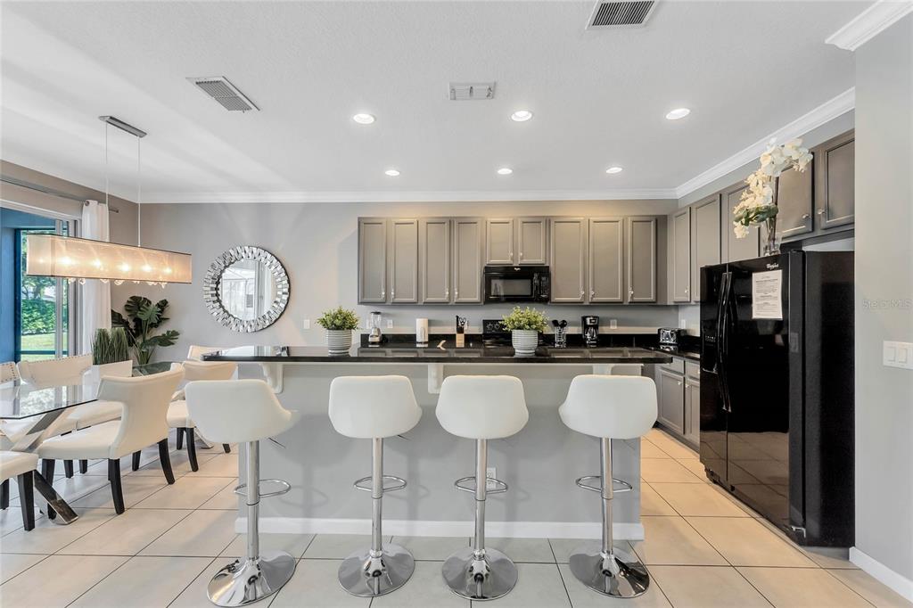 A kitchen features gray cabinets, a black countertop breakfast bar, and four white bar stools — 4348 ACORN COURT, DAVENPORT, FL