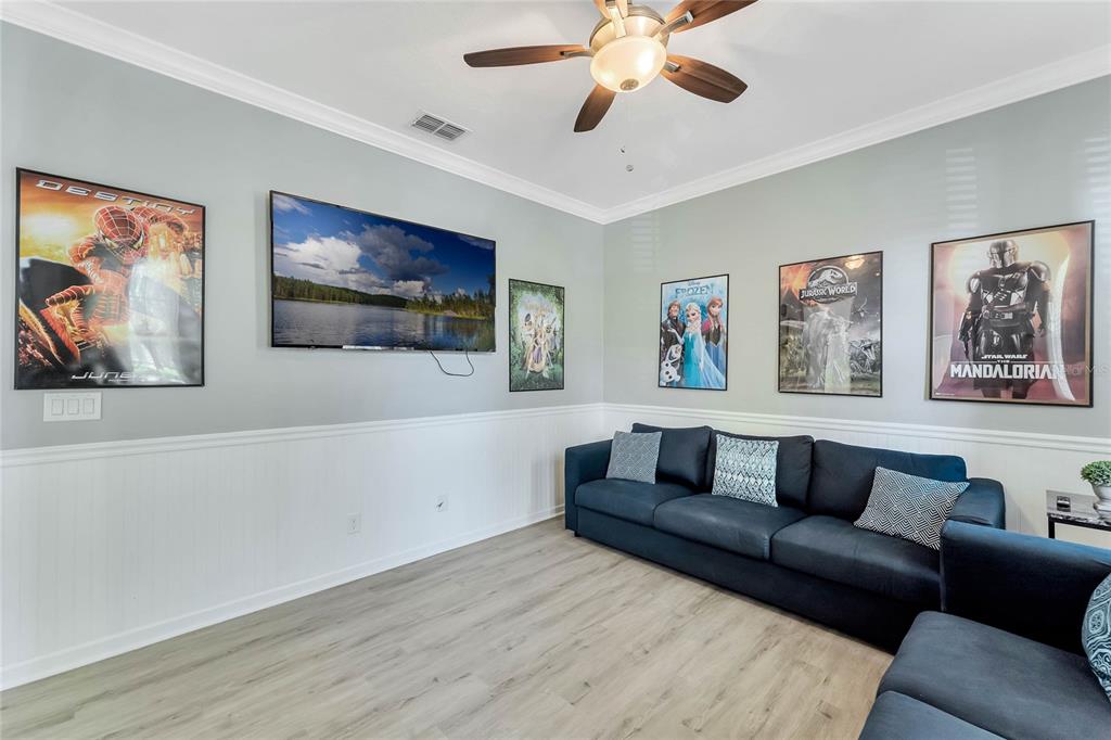 A living room features a dark blue sofa, a wall-mounted television, and several movie posters — 4348 ACORN COURT, DAVENPORT, FL