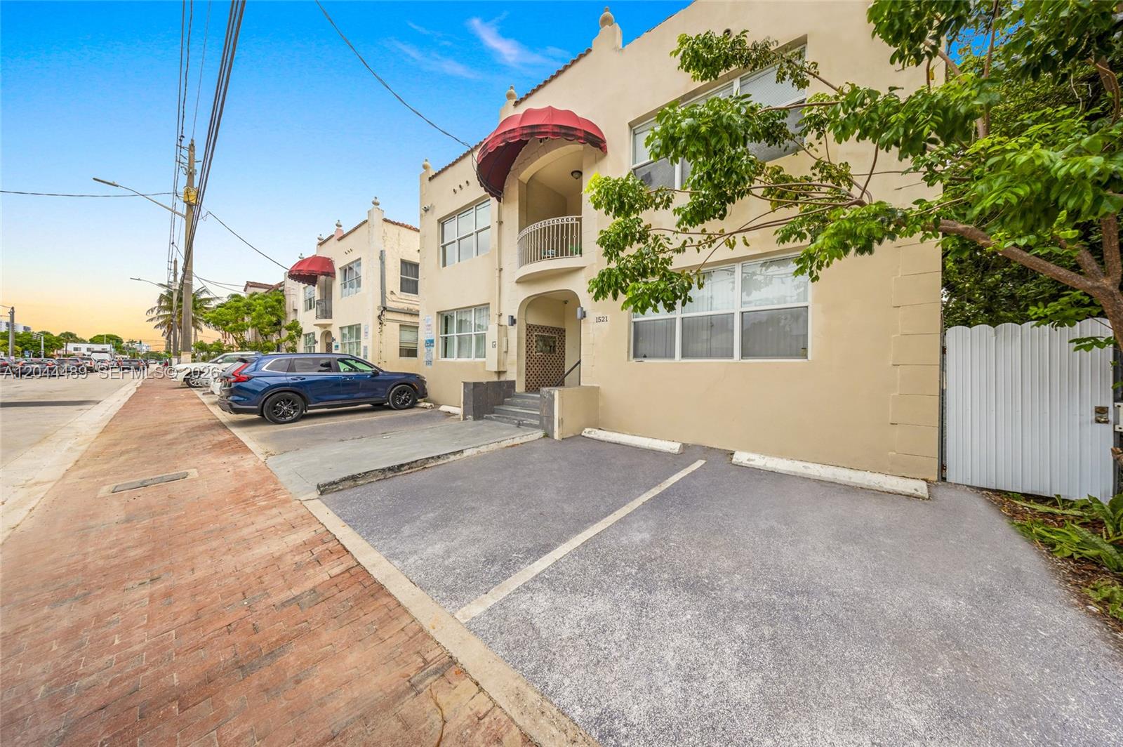 The exterior of a tan multi-story apartment building features red awnings and paved parking spaces — 1521 SW 7th St, Miami FL 33135, MIAMI, FL