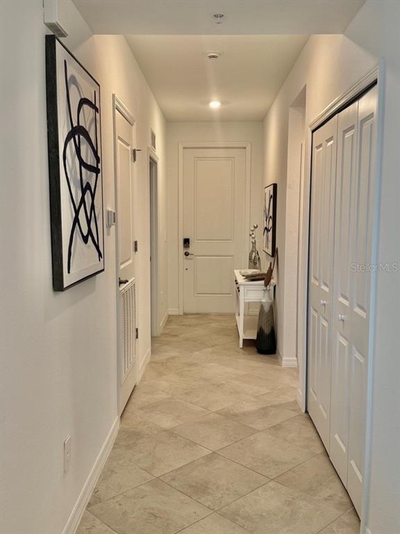 A hallway features tile flooring, white doors, a console table, and abstract wall art — 19116 SCALLOP LOOP UNIT 207, LAKEWOOD RANCH, FL