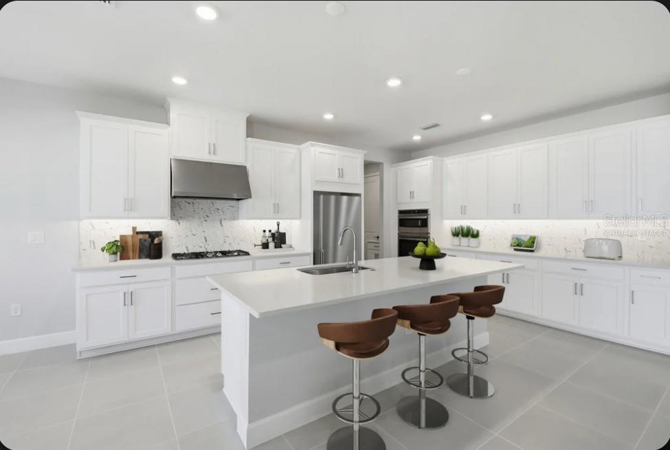 A modern kitchen features white cabinetry, a large central island with barstools, and marble countertops — 15993 HONEY HARVEST STREET, WINTER GARDEN, FL