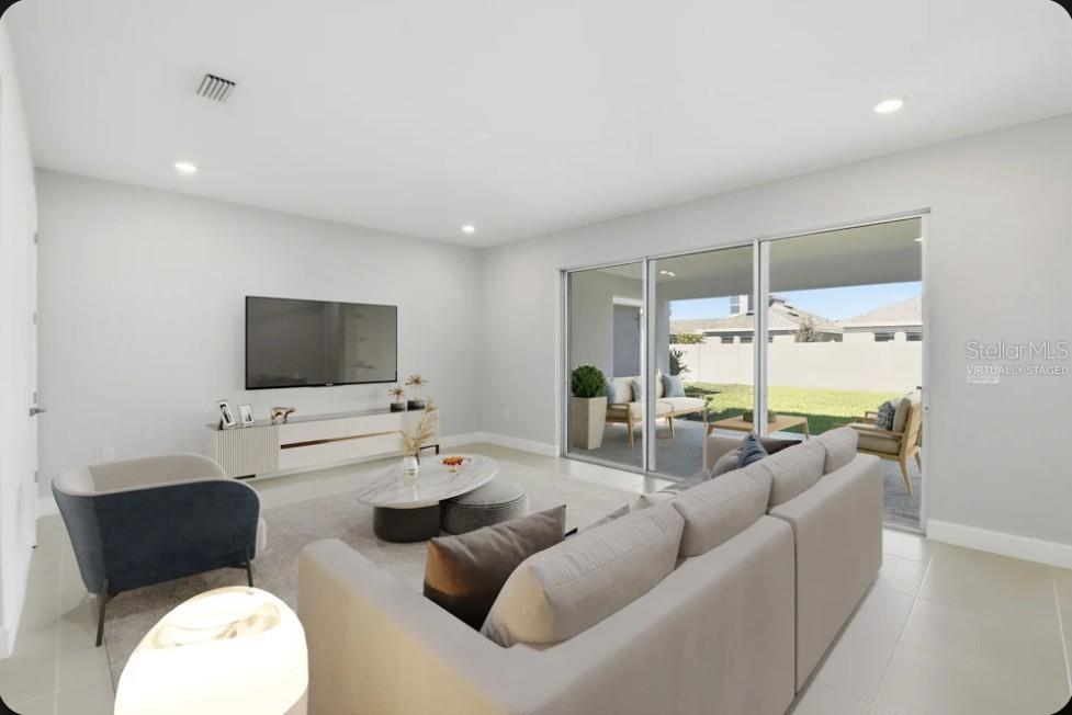 A living room with a large sofa, television, and sliding glass doors leading to a patio — 15993 HONEY HARVEST STREET, WINTER GARDEN, FL