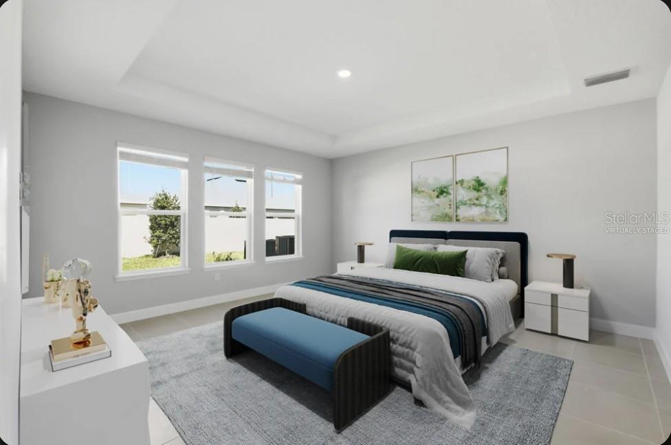 This virtually staged bedroom features a tray ceiling, large windows, and light-colored tile flooring — 15993 HONEY HARVEST STREET, WINTER GARDEN, FL