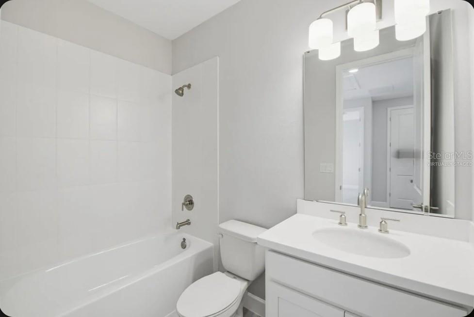 A bathroom features a white vanity, a toilet, and a bathtub with a tiled surround — 15993 HONEY HARVEST STREET, WINTER GARDEN, FL