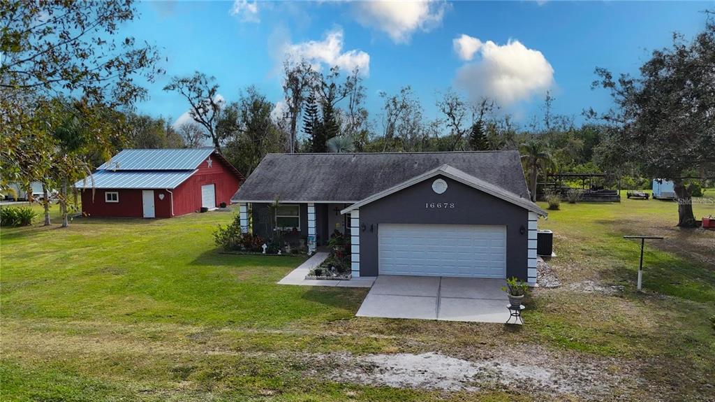 A grey house with a two-car garage sits next to a red barn on grass — 16678/16620 WATERLINE ROAD ROAD, BRADENTON, FL