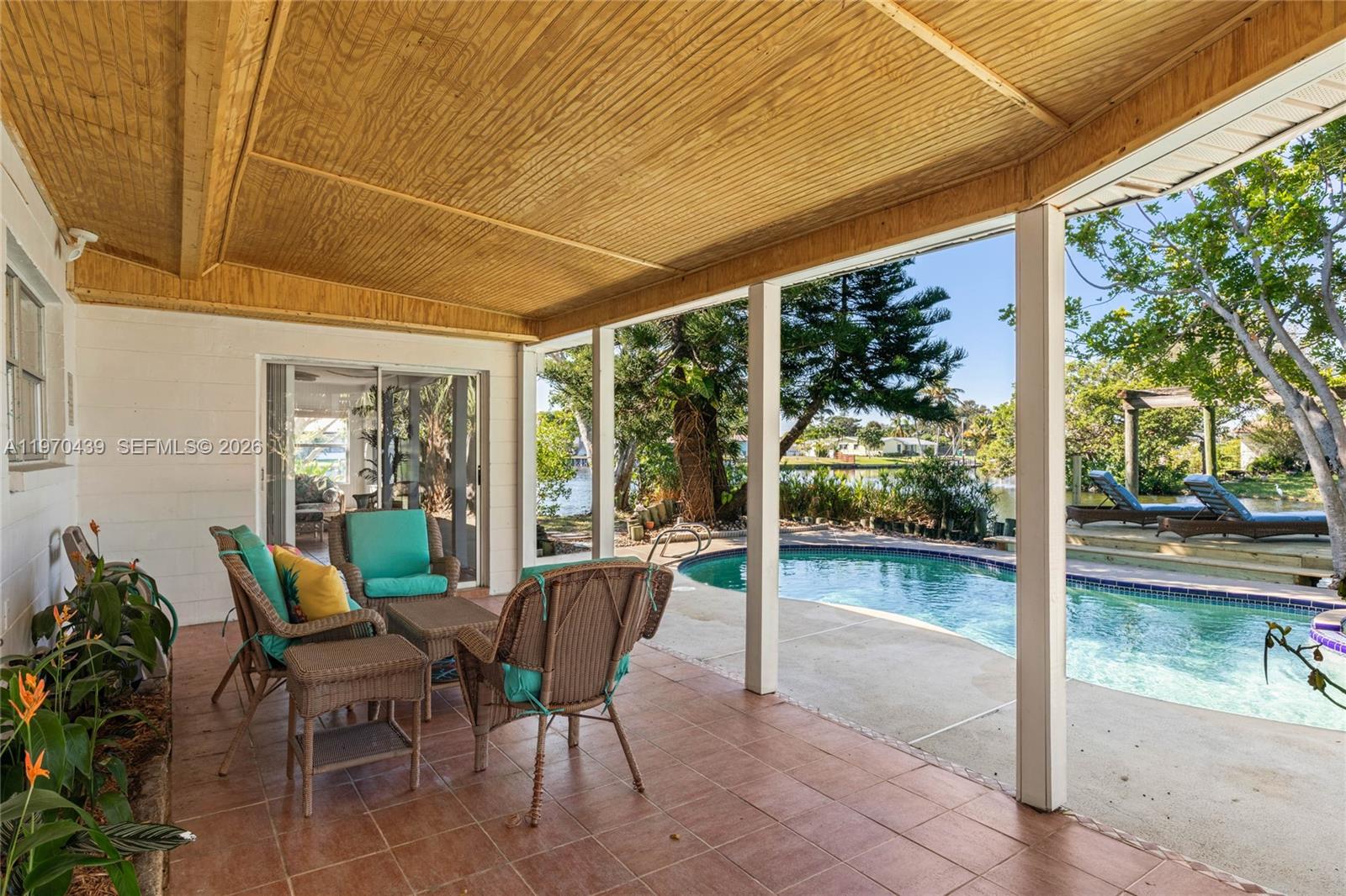 A covered patio with tiled flooring overlooks a swimming pool and a waterfront backyard — 124 Aucila RD., Cocoa Beach FL 32931, COCOA BEACH, FL