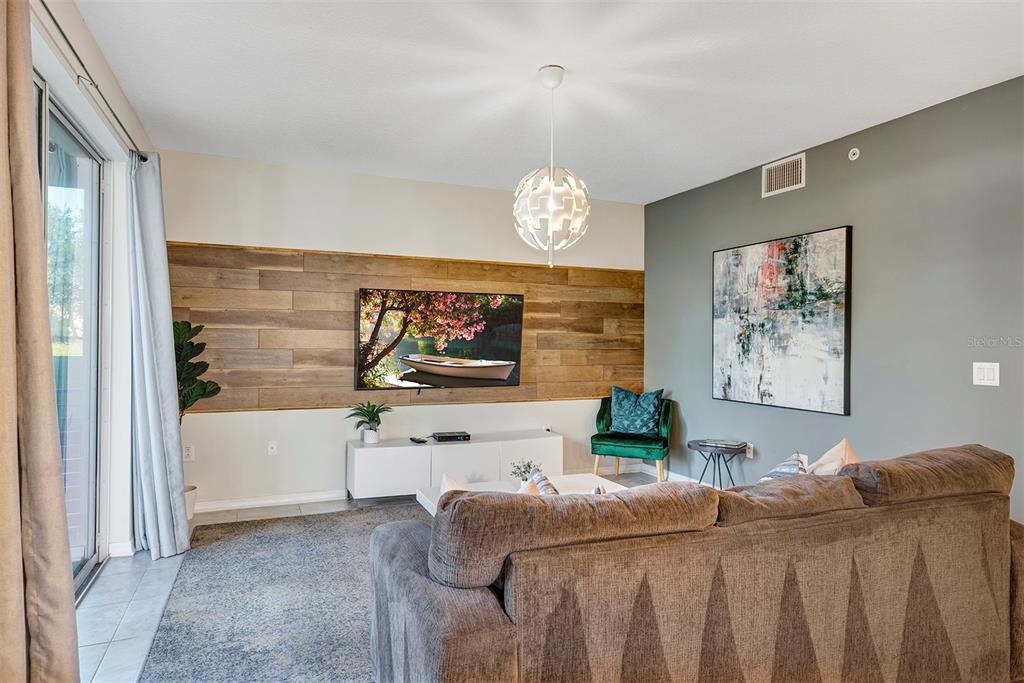 A living room features a wood-paneled accent wall, a television, and a gray sofa — 4751 CLOCK TOWER DRIVE UNIT 107, KISSIMMEE, FL