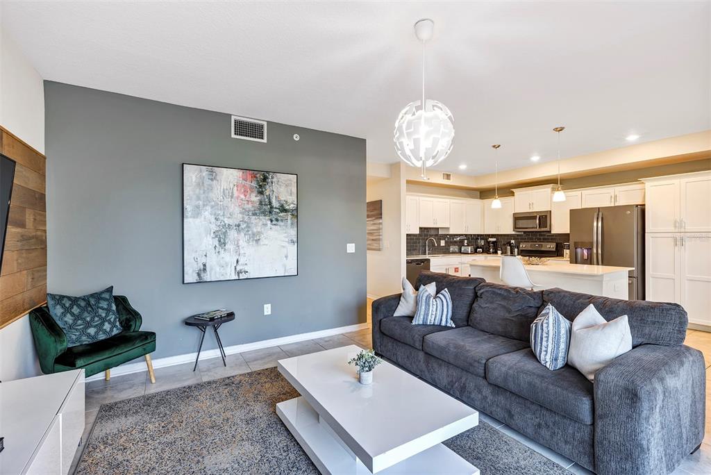 A living room with a grey sofa, white coffee table, and an open kitchen area — 4751 CLOCK TOWER DRIVE UNIT 107, KISSIMMEE, FL