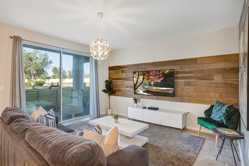 A living room features a wood-paneled accent wall, a white media console, and sliding doors — 4751 CLOCK TOWER DRIVE UNIT 107, KISSIMMEE, FL