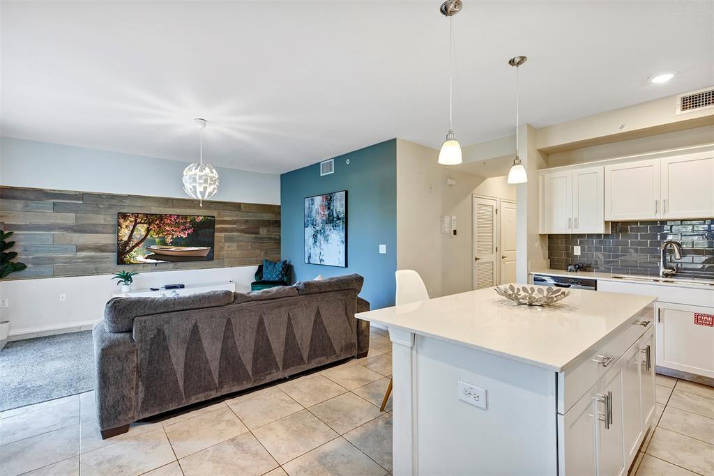 An open-concept living room and kitchen featuring a wood-paneled accent wall and a kitchen island — 4751 CLOCK TOWER DRIVE UNIT 107, KISSIMMEE, FL