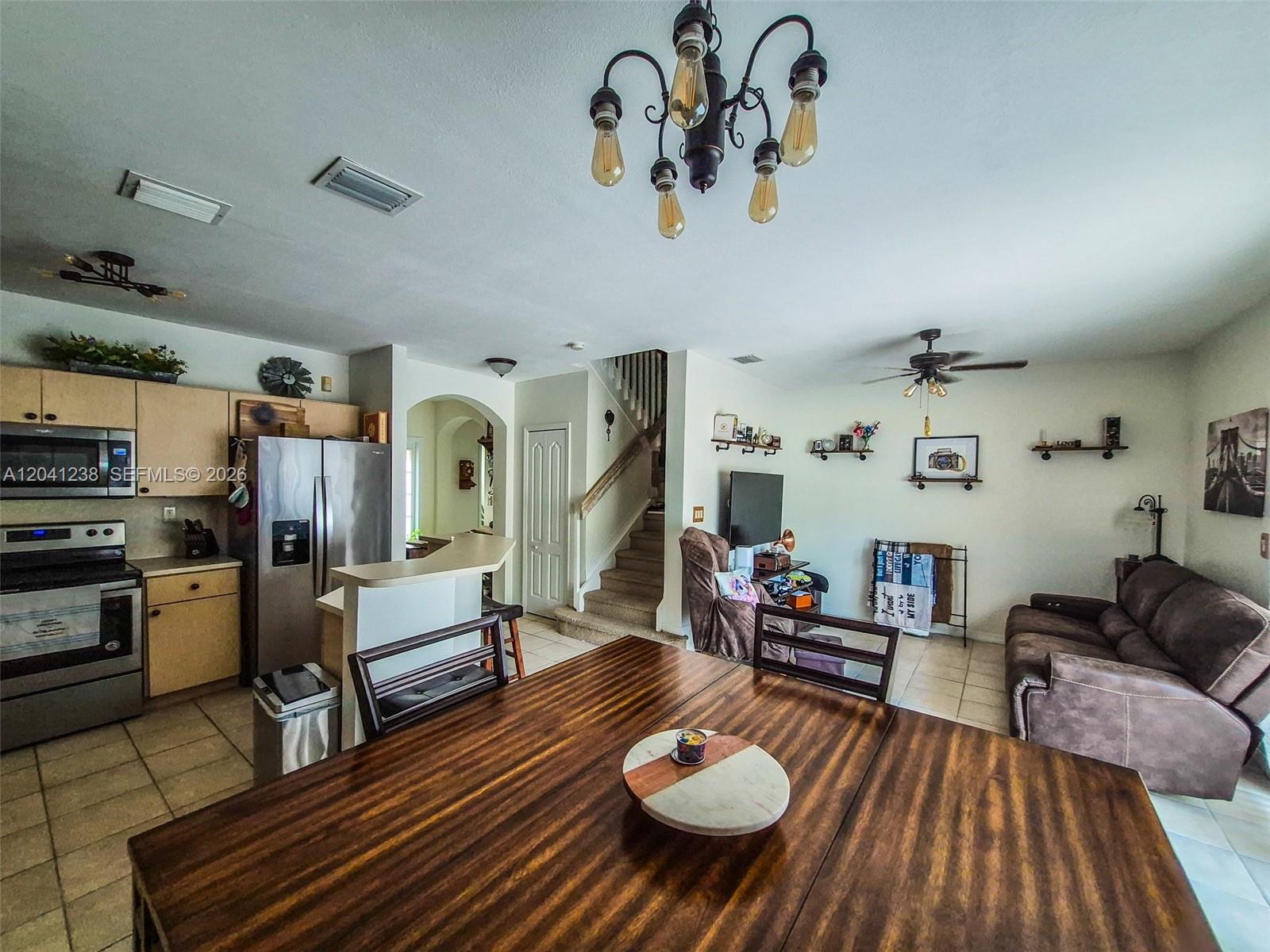 A kitchen and living area featuring a wooden dining table, stainless appliances, and a staircase — 12850 SW 28th Ct, Miramar FL 33027, MIRAMAR, FL