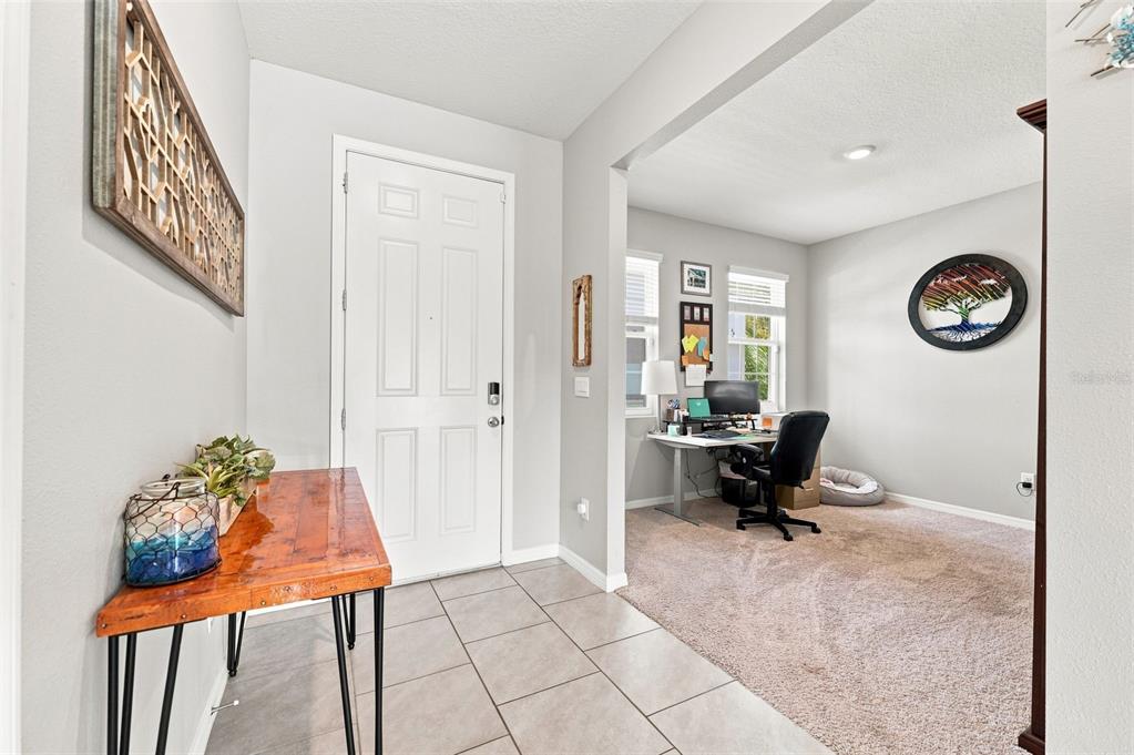An entryway with tile flooring leads into a carpeted home office with a desk — 8673 BOWER BASS CIRCLE, WESLEY CHAPEL, FL