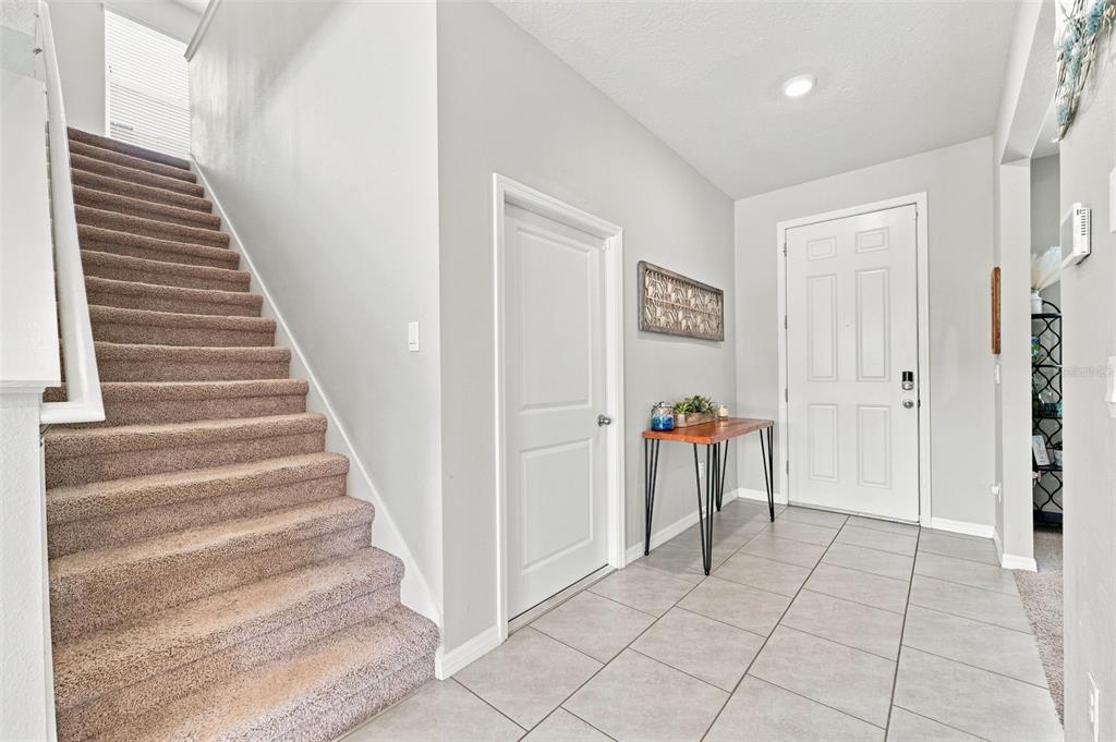 An entryway features a carpeted staircase, a white door, and a small wooden console table — 8673 BOWER BASS CIRCLE, WESLEY CHAPEL, FL