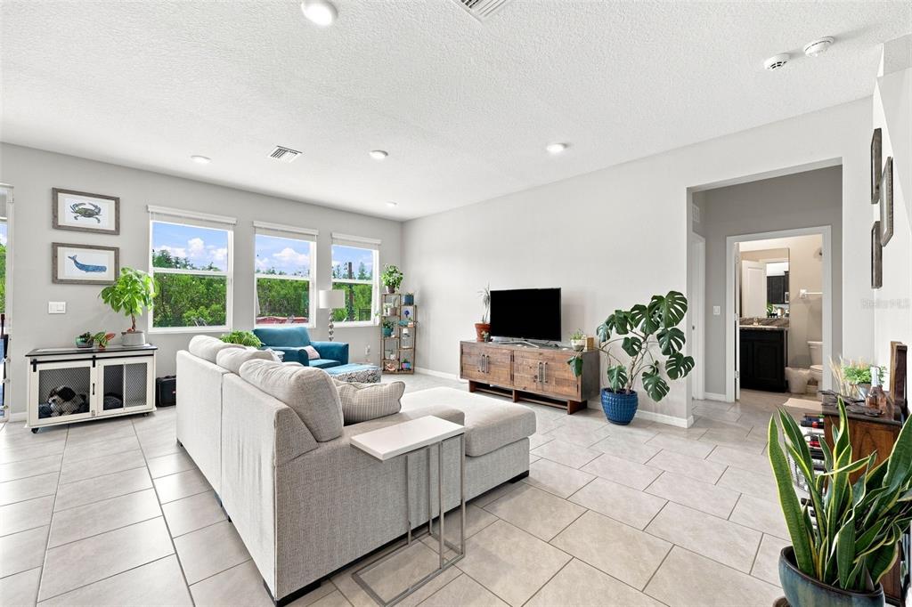 A living room features a gray sectional sofa, a television on a wooden console, and tile flooring — 8673 BOWER BASS CIRCLE, WESLEY CHAPEL, FL