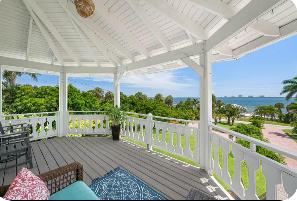 A covered wooden deck with white railings overlooks a lush landscape and the ocean — 12417 S Indian River Drive, Jensen Beach FL 34957, JENSEN BEACH, FL