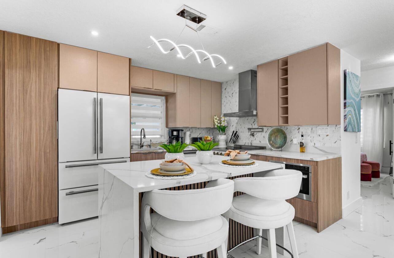 A modern kitchen features a white marble island, light wood cabinets, and stainless steel appliances — 12417 S Indian River Drive, Jensen Beach FL 34957, JENSEN BEACH, FL