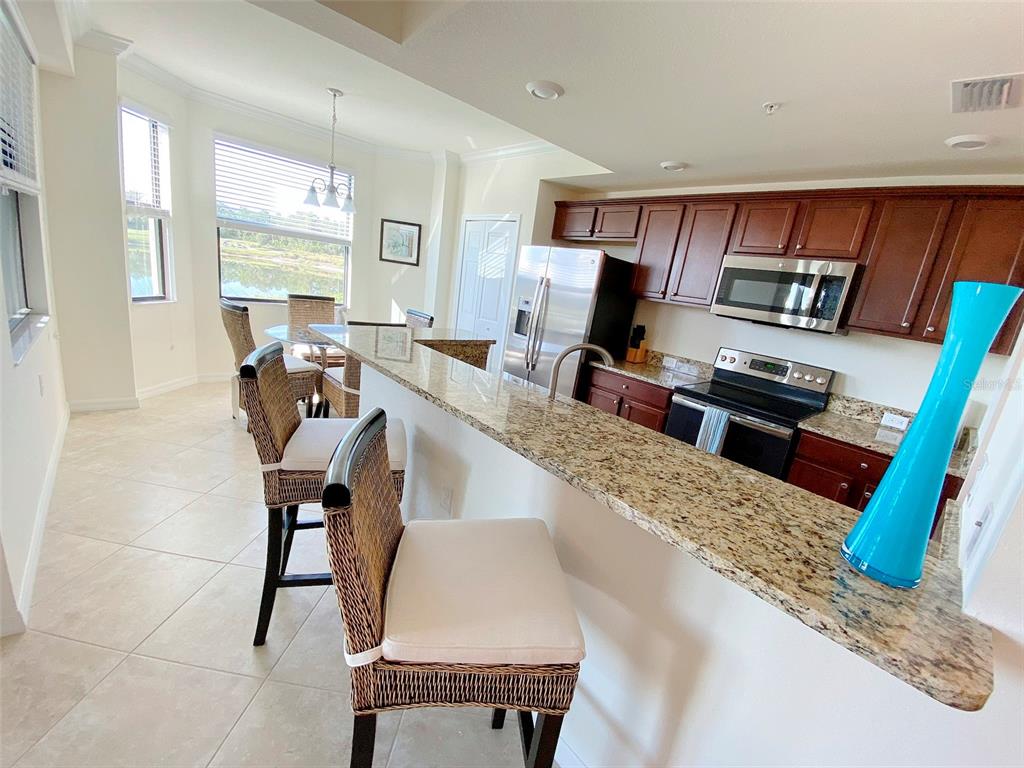 A kitchen with granite countertops, dark wood cabinets, and a breakfast bar with wicker chairs — 16706 VARDON TERRACE UNIT 102, BRADENTON, FL