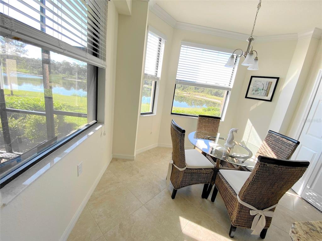 A breakfast nook features a glass-topped table, wicker chairs, tile floors, and lake views — 16706 VARDON TERRACE UNIT 102, BRADENTON, FL