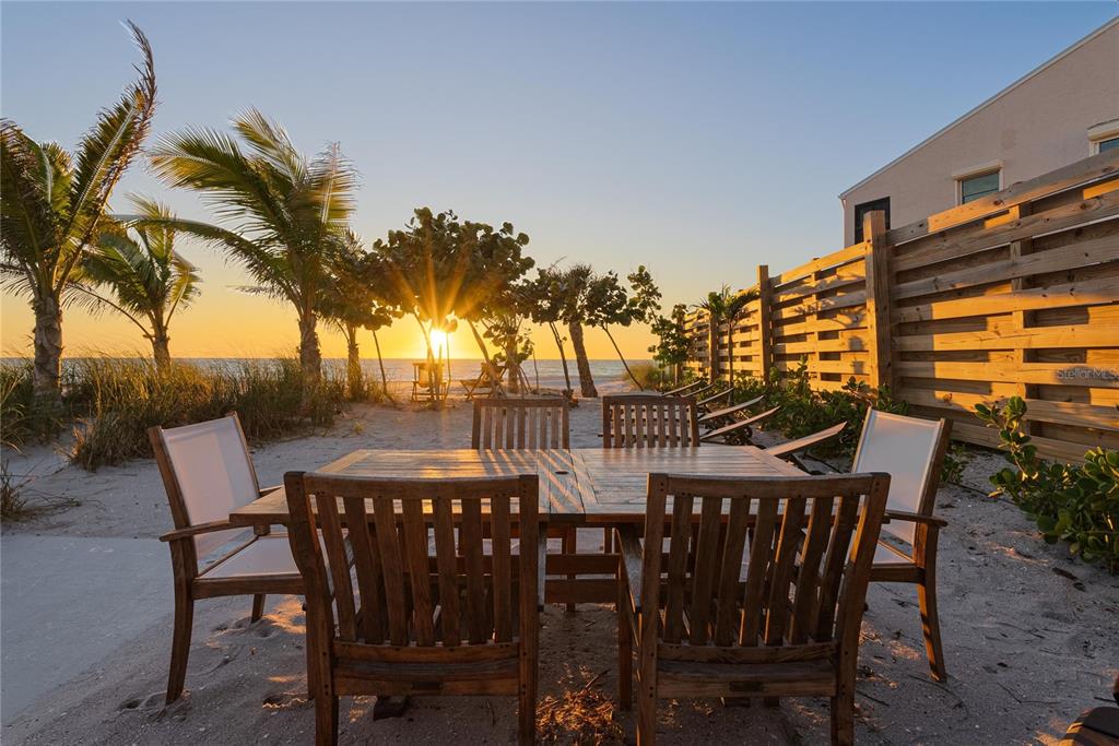 A wooden dining set sits on a sandy beach at sunset next to a privacy fence — 2630 N BEACH ROAD, ENGLEWOOD, FL