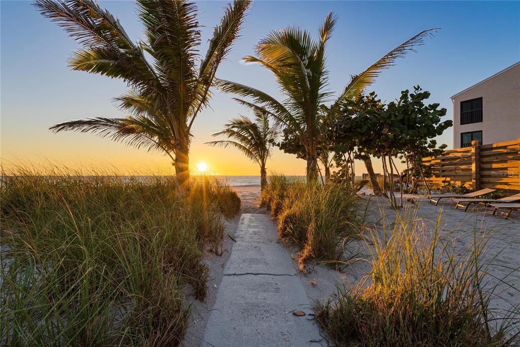 A concrete path leads through beach grass toward the ocean at sunset with palm trees — 2630 N BEACH ROAD, ENGLEWOOD, FL