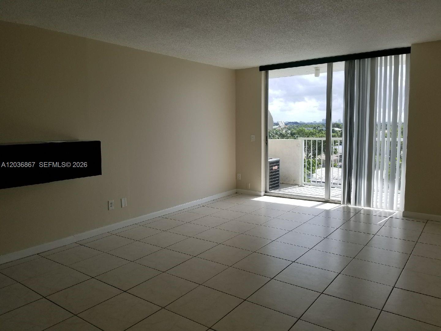 An empty room features light-colored tile flooring, a wall-mounted black shelf, and a sliding glass door — NORTH MIAMI, FL