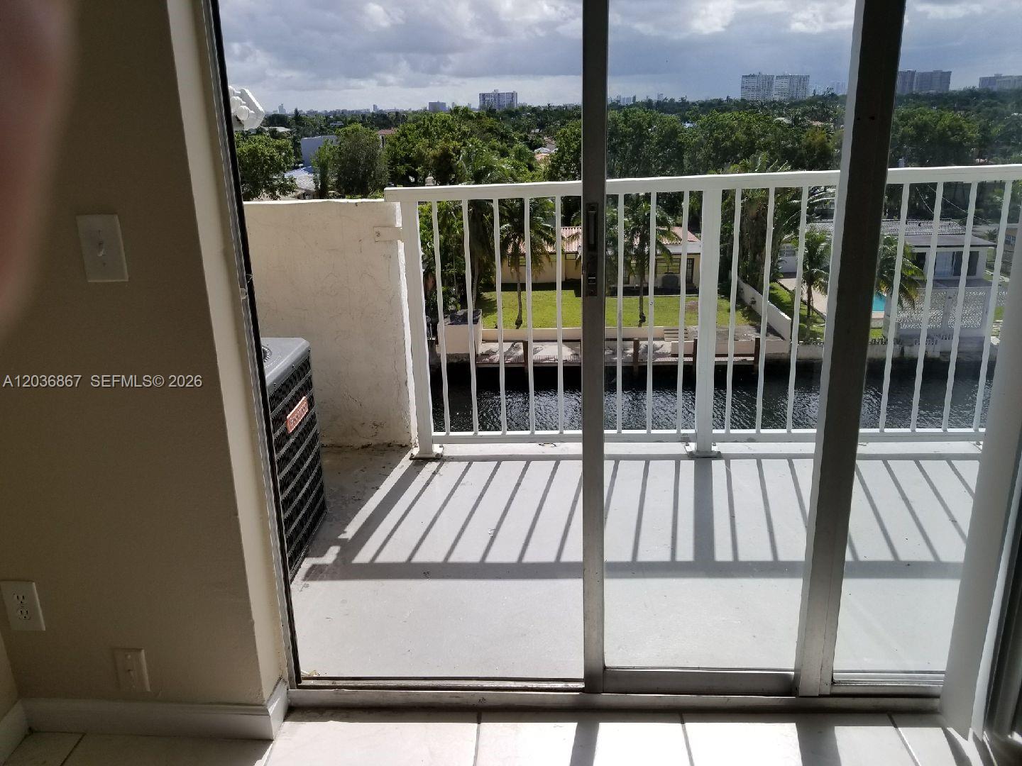 A balcony with a metal railing overlooks a canal, trees, and distant city buildings — NORTH MIAMI, FL