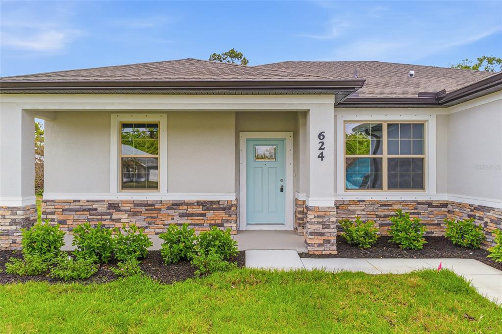 The exterior of a single-story house features a light blue front door and stone siding — 2624 ATWATER DRIVE, NORTH PORT, FL