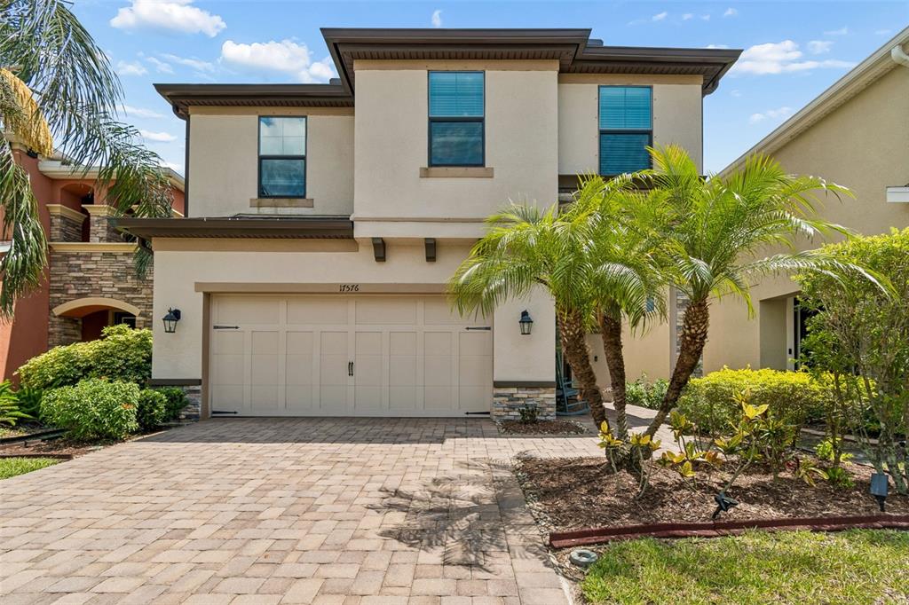 A two-story house with a beige stucco exterior, a two-car garage, and a palm tree — 17576 TERRAZZO WAY, LAND O LAKES, FL