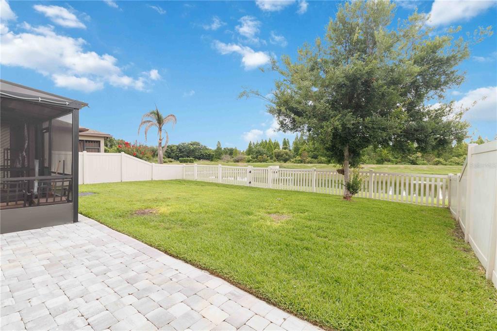 A backyard with a paved patio, a grassy lawn, and a white vinyl fence — 11415 BLUE CRANE STREET, RIVERVIEW, FL