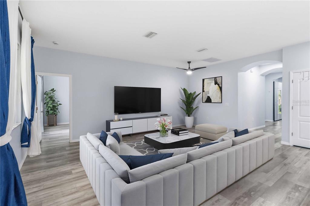 A living room features a large sectional sofa, a television, and light wood-look flooring — 11415 BLUE CRANE STREET, RIVERVIEW, FL