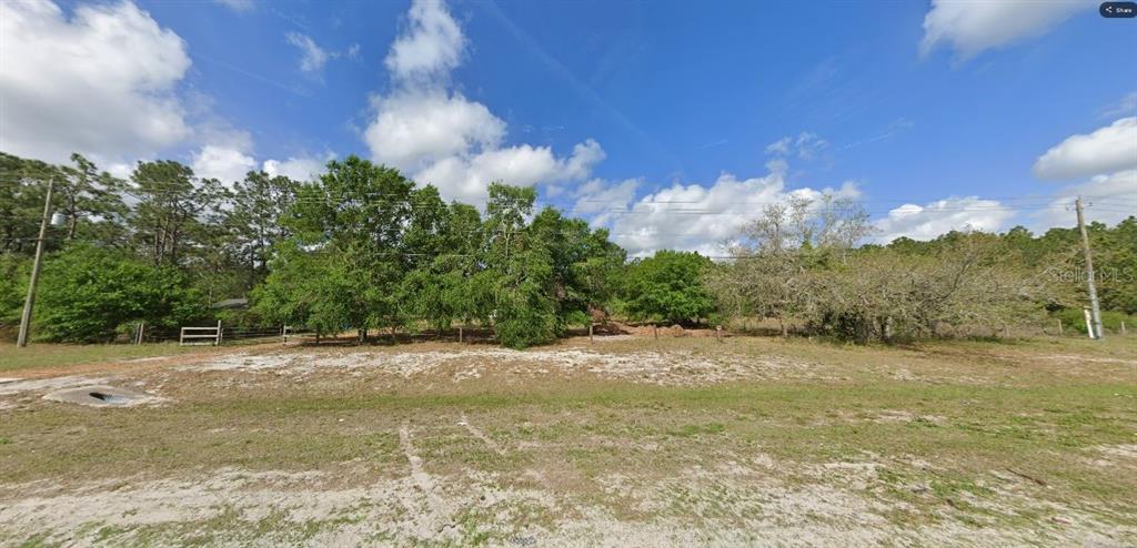 A vacant, grassy lot with scattered trees and a fence under a blue sky — COMMONWEALTH AVE N, POLK CITY, FL